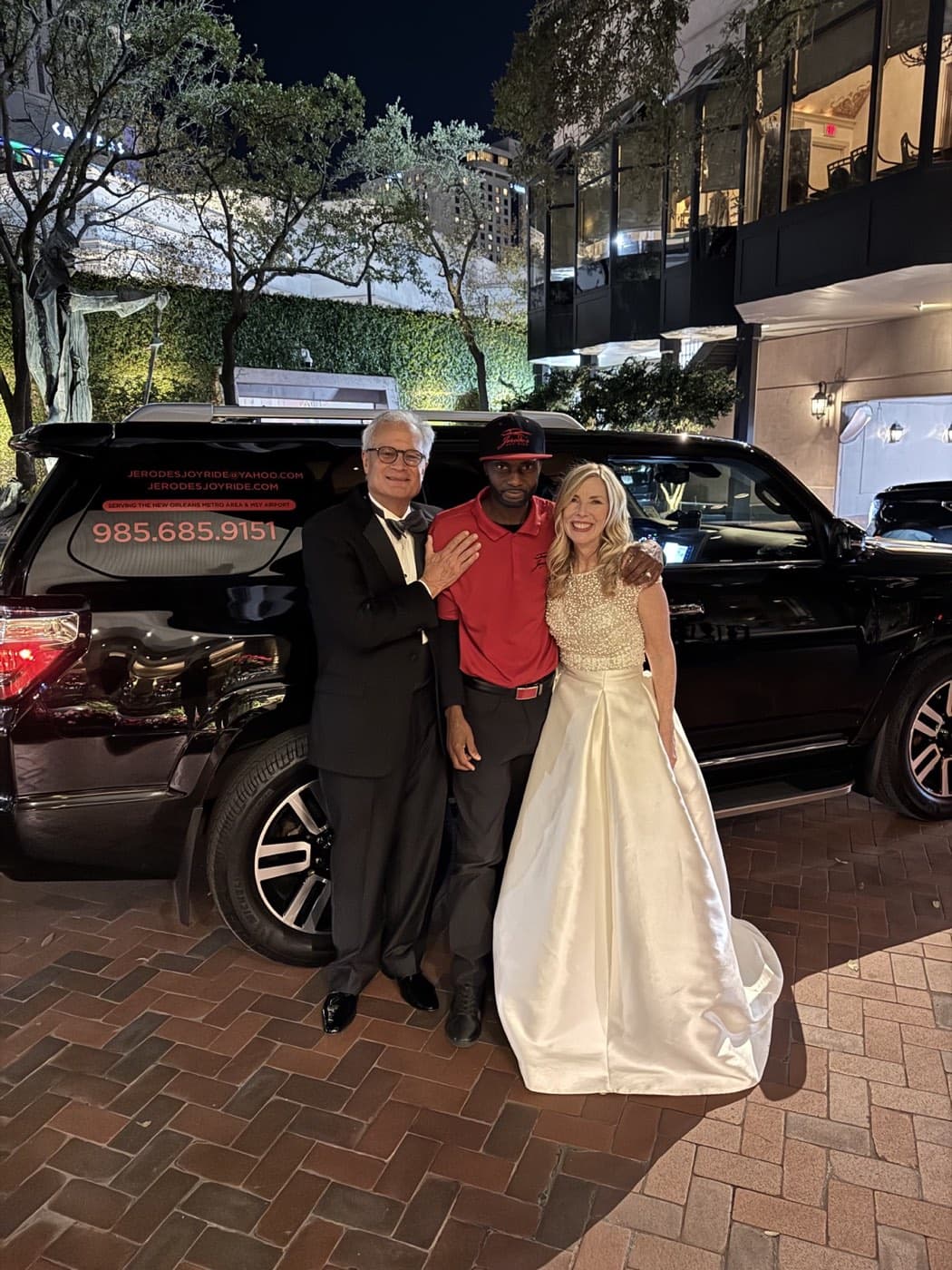Jerode with a newly married couple beside the black SUV